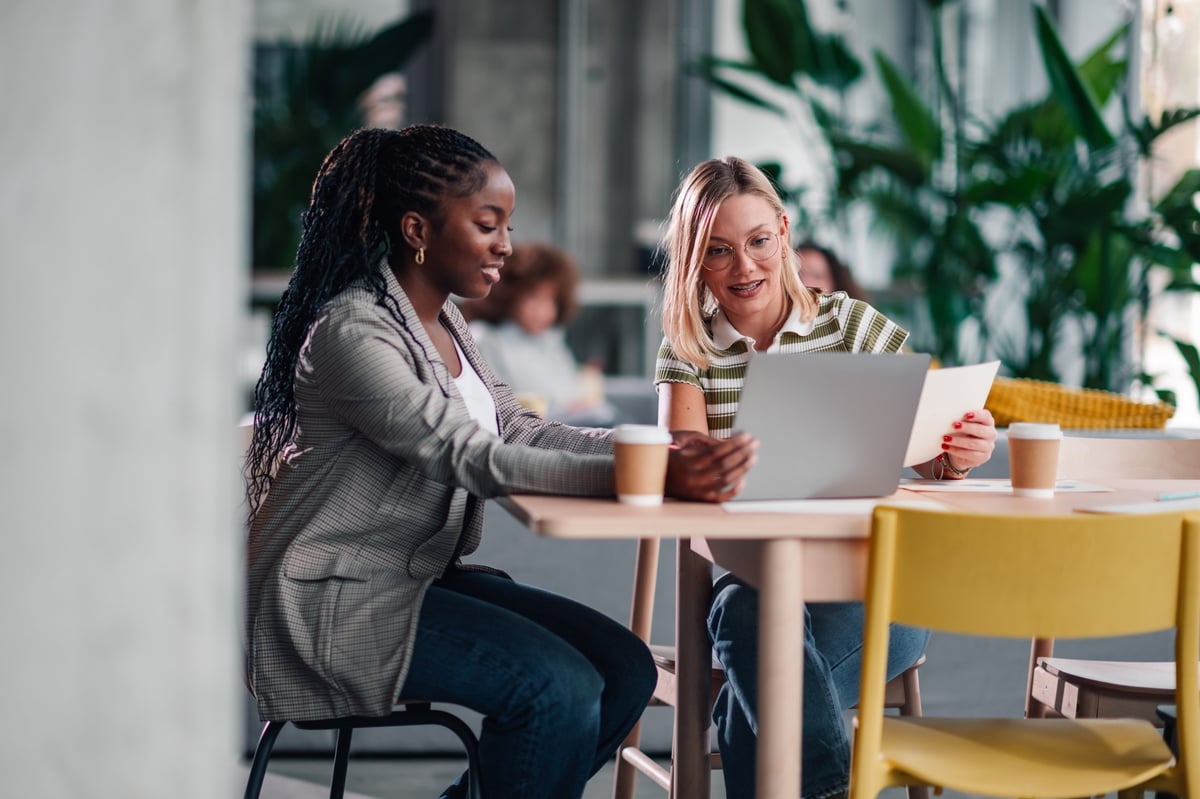 Two women colleagues working together, discussing project details on a laptop at a modern coworking office space